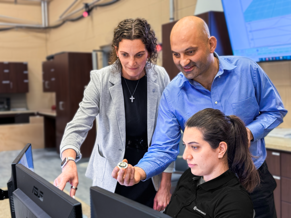 Three people lean over a computer.